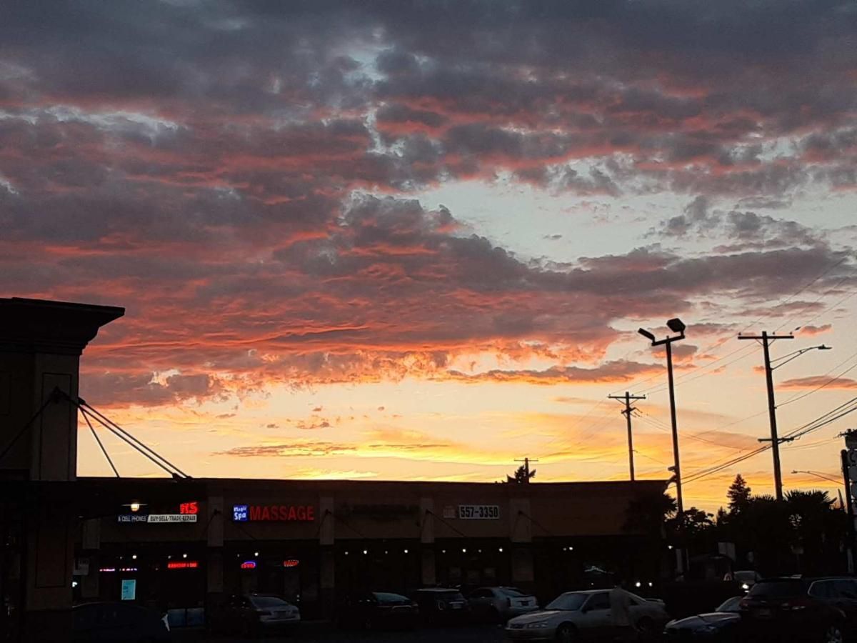 A sunset with pink and orange clouds above a suburban shopping center parking lot.