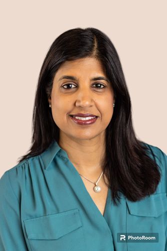 Portrait of a smiling woman in a teal blouse against a light beige background.