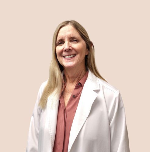 Smiling healthcare professional in a white coat over a pink blouse against a plain beige background