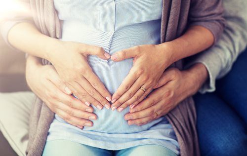Couple's hands forming a heart on a pregnant belly.
