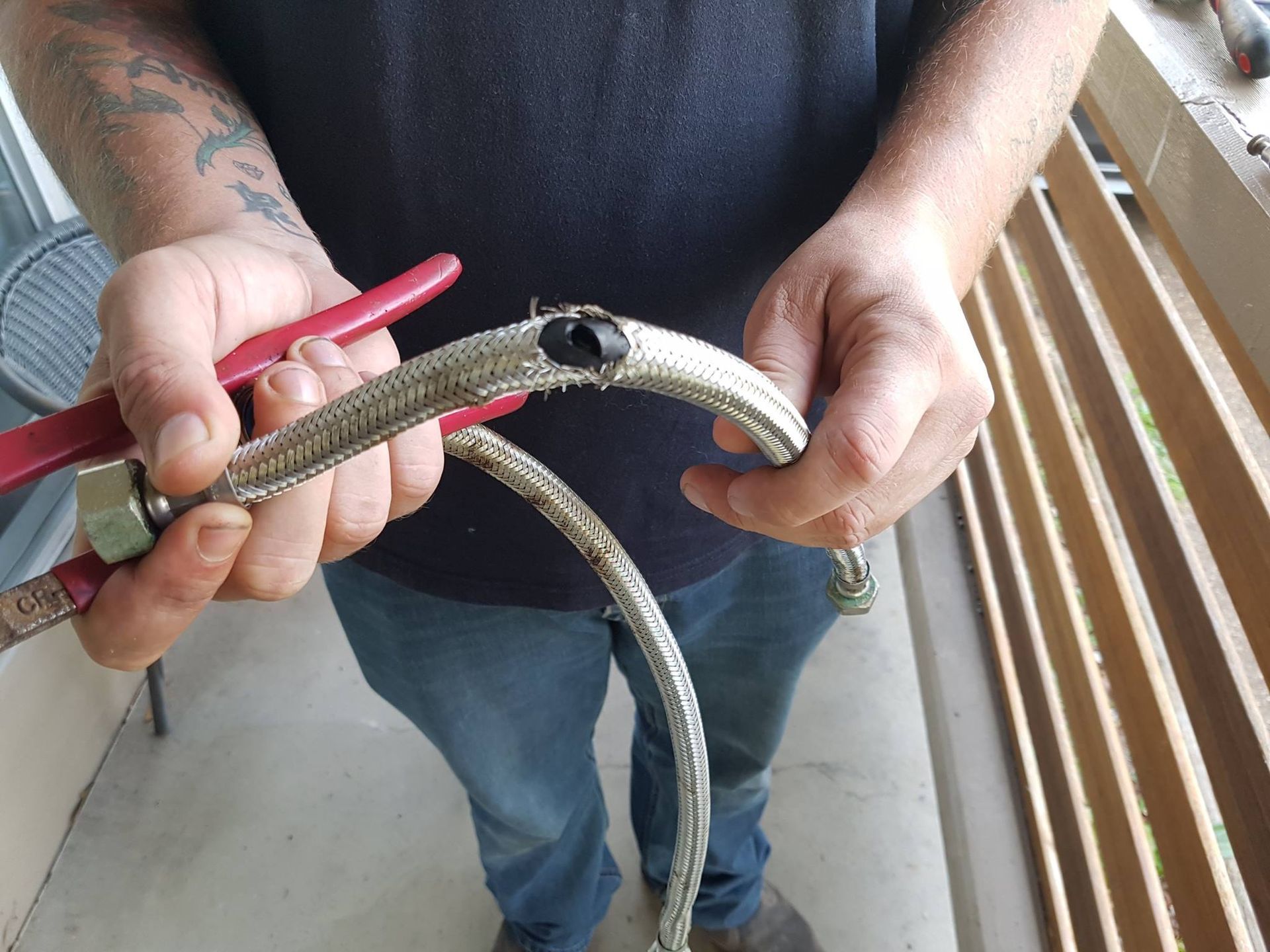 Person Holding a Broken, Silver Braided Hose With Pliers, Outdoors — Hunter Plumbing And Hotwater in Raymond Terrace, NSW