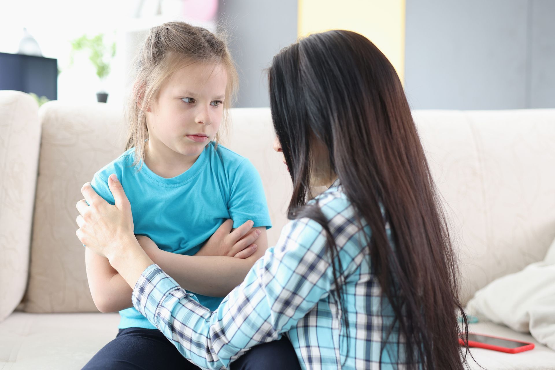 Woman comforts child on couch, child has arms crossed, appears upset.