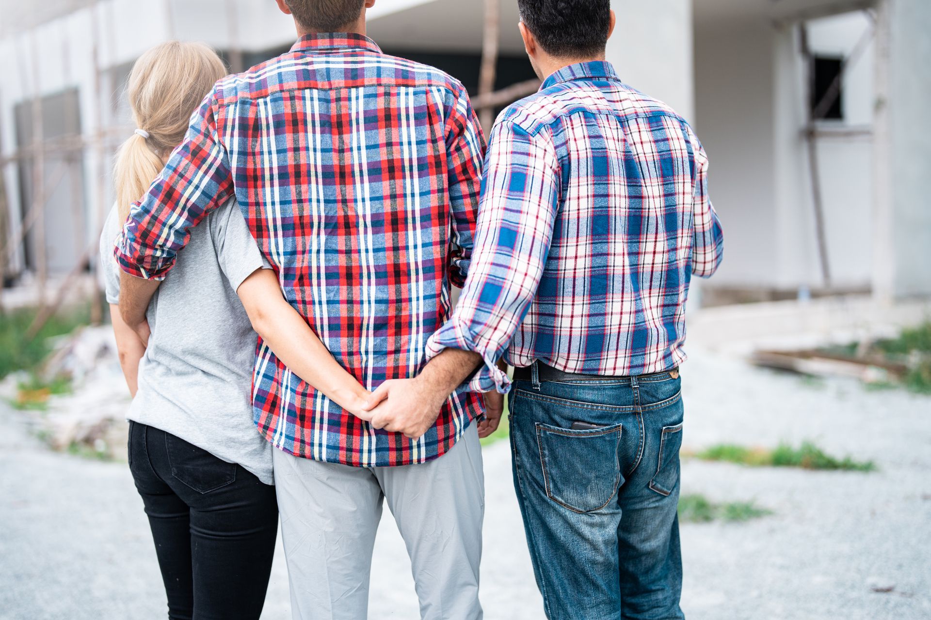 Three people holding hands, outdoors; one with blonde hair, the others in plaid shirts.