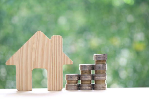 Wooden house silhouette beside a stack of coins, symbolizing financial growth and homeownership.