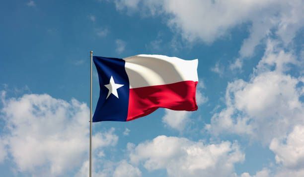 Texas flag waving against a bright blue sky with white clouds.