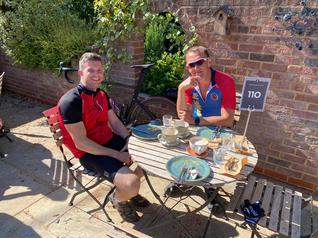Jason Jennings and a friend outside at a cafe wearing cycle gear