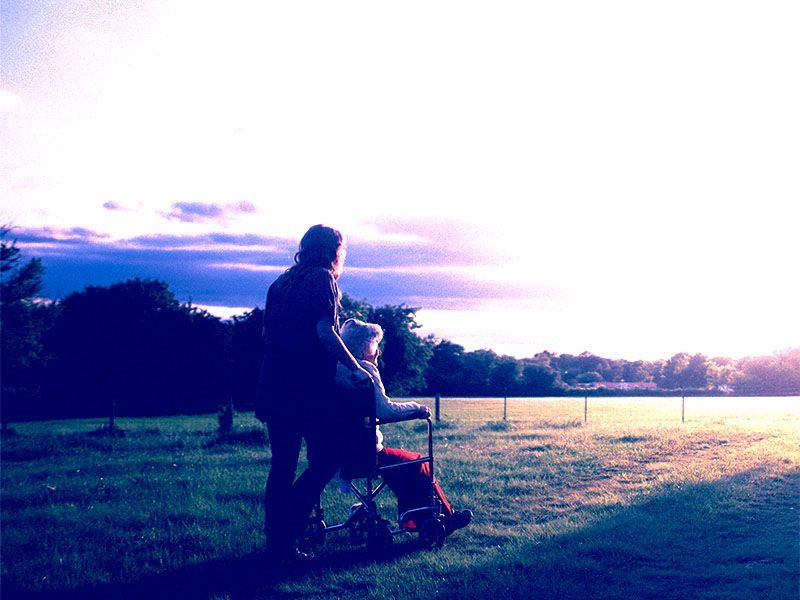 Carer pushing a service user in a wheelchair through a rural setting