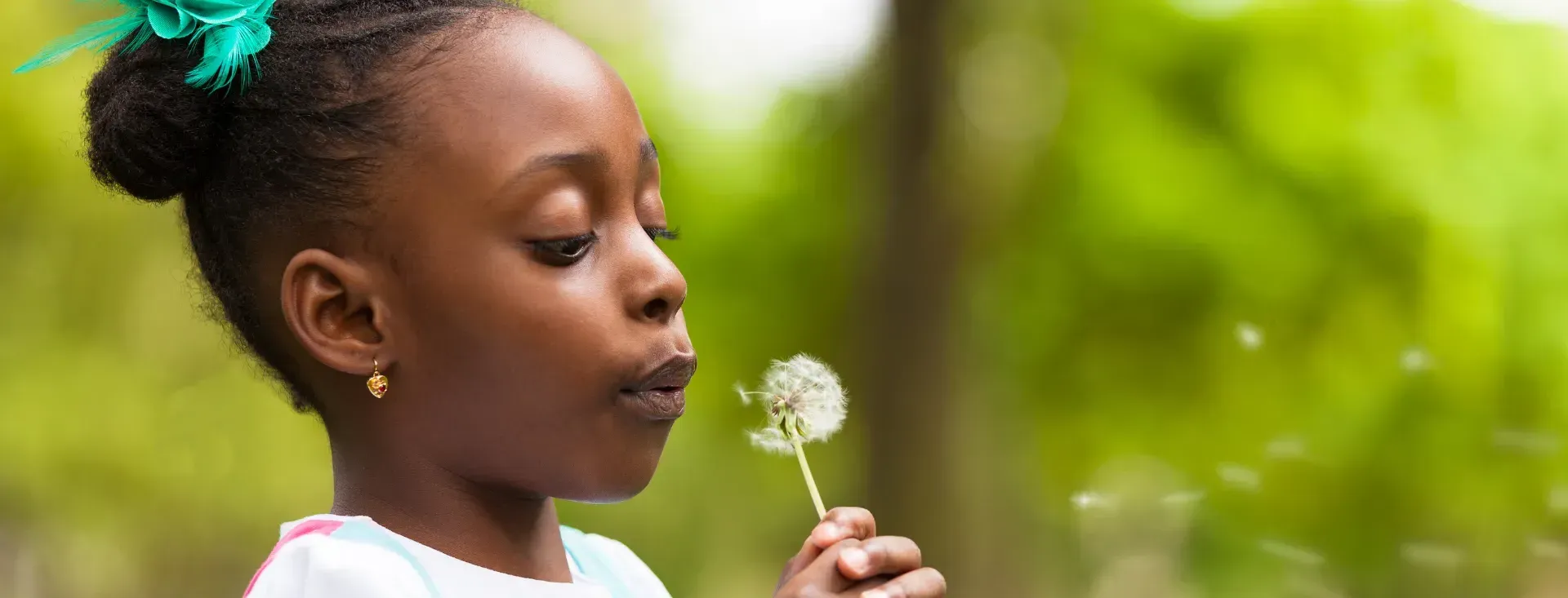 A little girl is blowing a dandelion in the air.