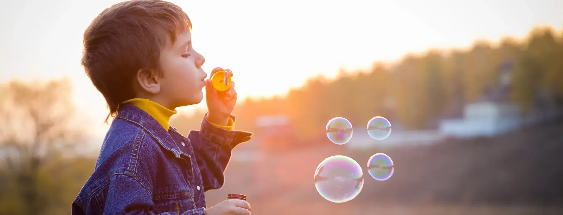 Boy blowing bubbles at dusk in a park.