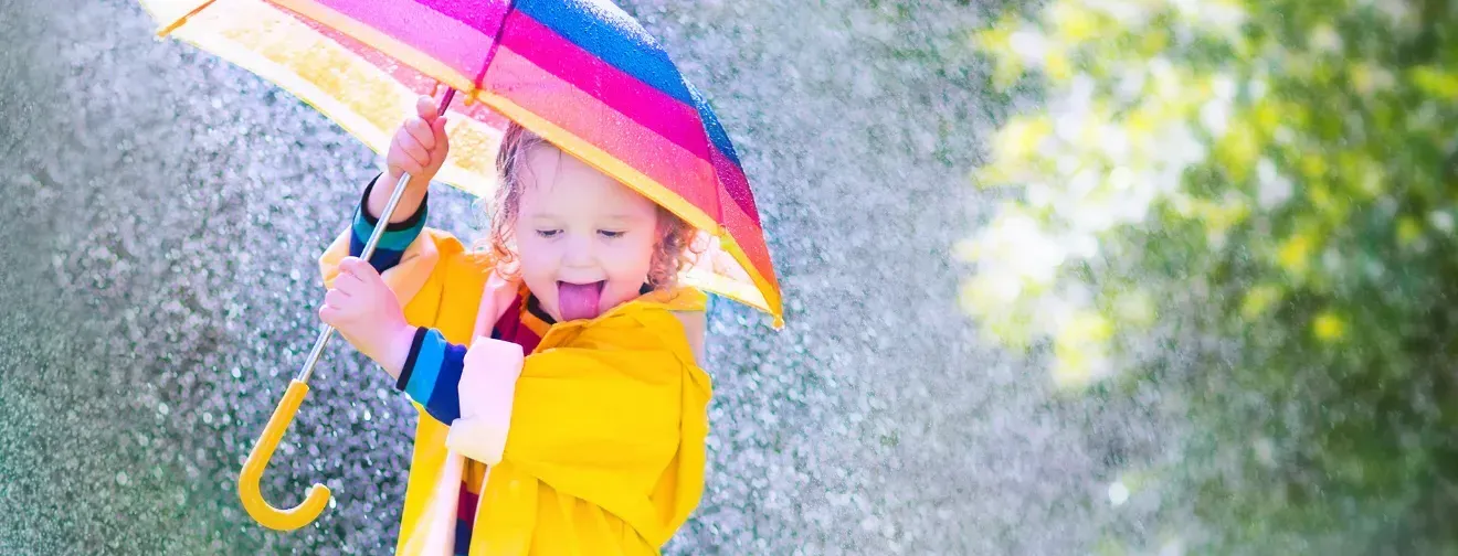 A little girl in a yellow raincoat is holding a colorful umbrella in the rain.