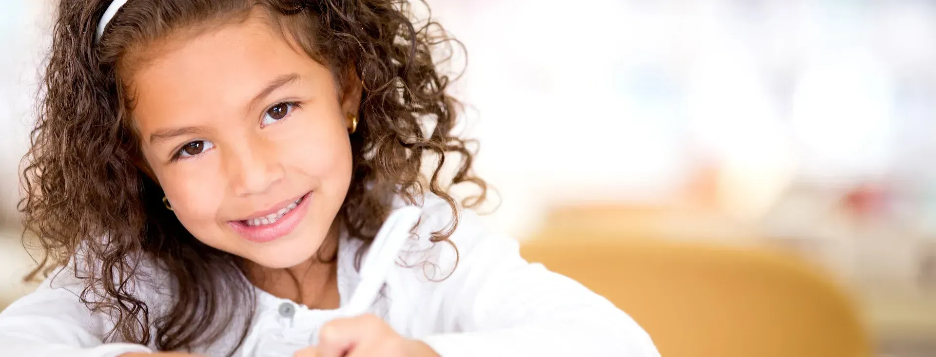 A little girl with curly hair is smiling while sitting at a desk.