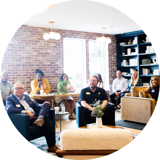 People in a room with brick wall, conversing, seated in chairs, and near a table.