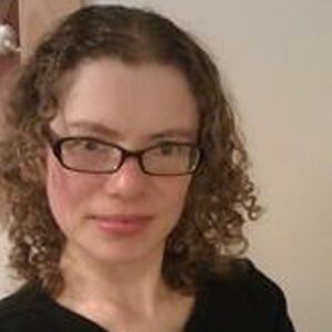 Woman with curly brown hair wearing glasses, smiling.