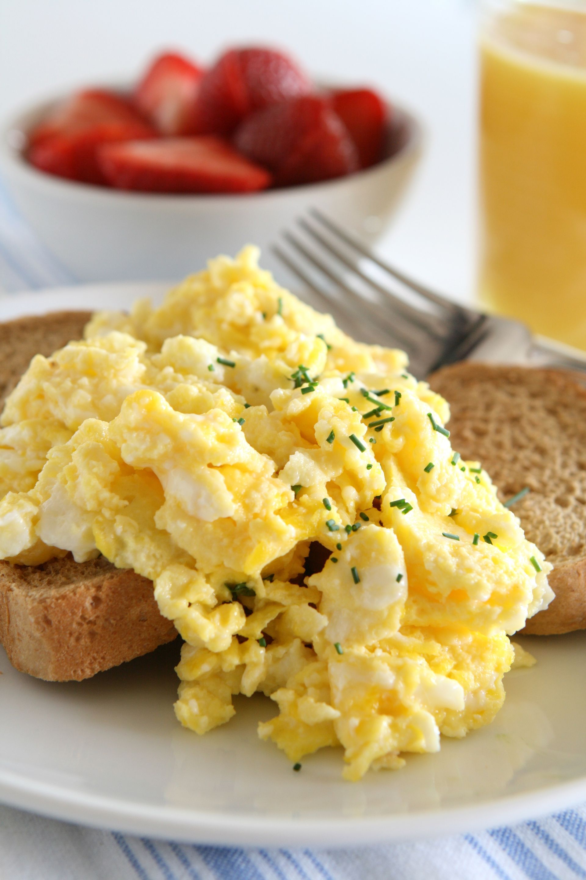 Scrambled eggs on toast with berries and orange juice on a breakfast plate