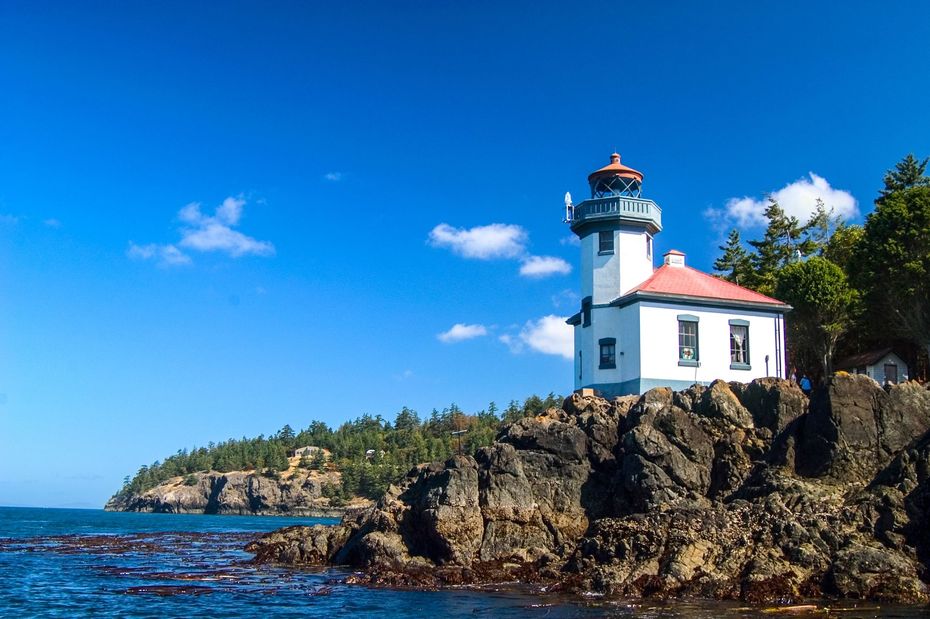 White lighthouse on rocky coast under a bright blue sky, with ocean and cliffs in the background