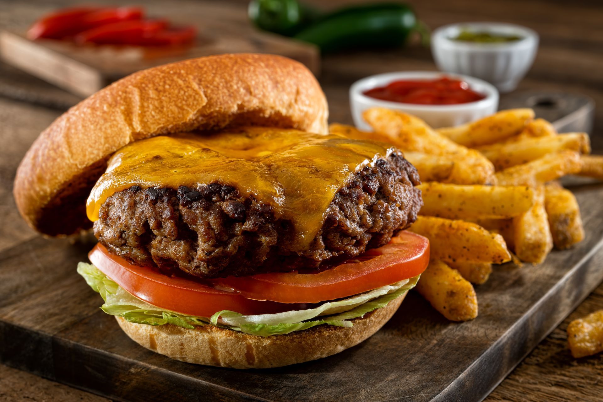 Cheeseburger on a bun with lettuce, tomato, fries, and dipping sauces on a wooden board