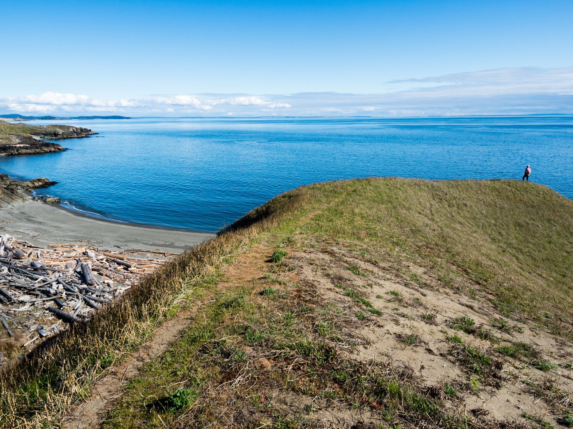 Coastal grassy bluff overlooking a calm blue bay under a clear sky