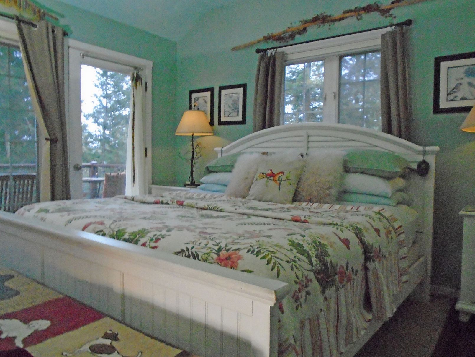 Bright bedroom with a white bed, floral quilt, green walls, and windows letting in daylight