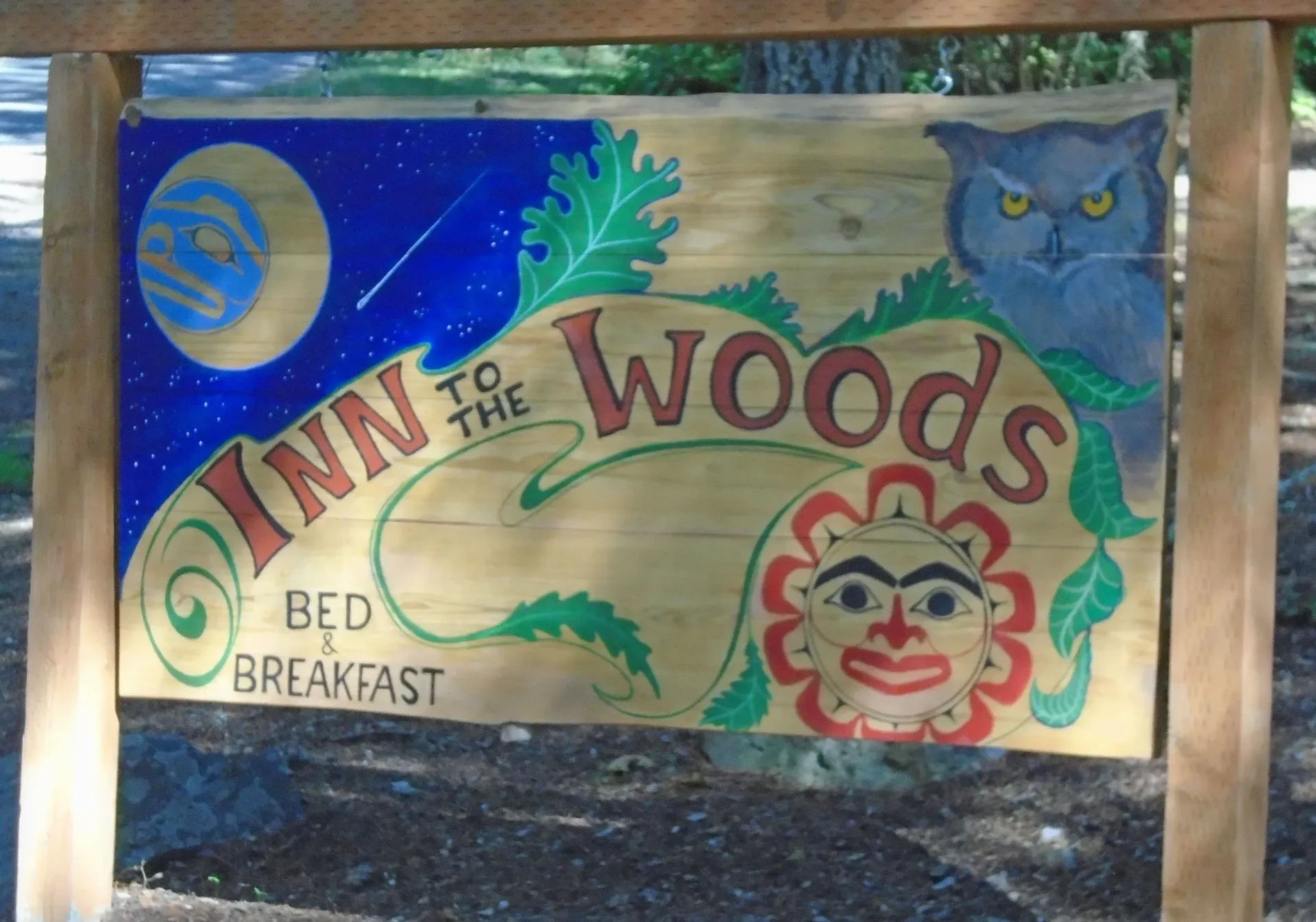 Hand-painted sign for Inn to the Woods bed and breakfast with moon, owl, tree, and sun face under wood frame