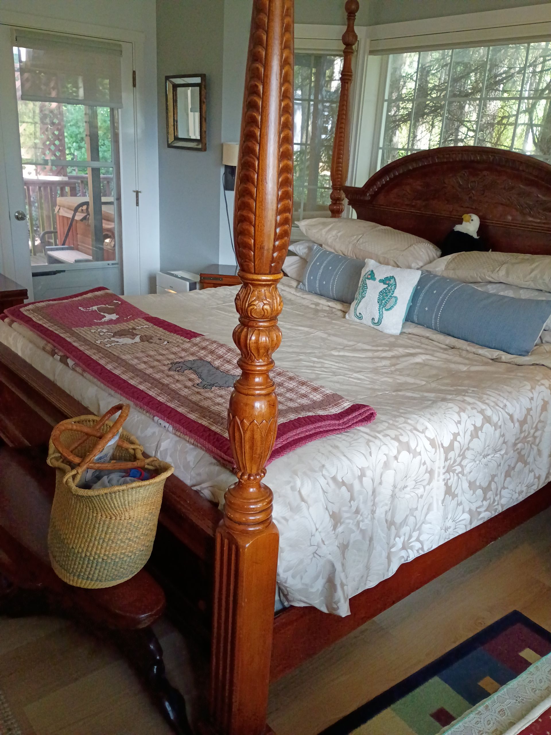 Bedroom with a wooden four-poster bed, white bedding, red runner, and wicker basket by a bright window