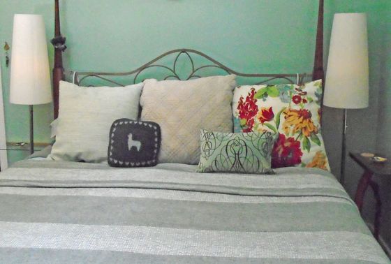 Neatly made bed with gray bedding, white pillows, and colorful floral accent pillow beside two lamps.