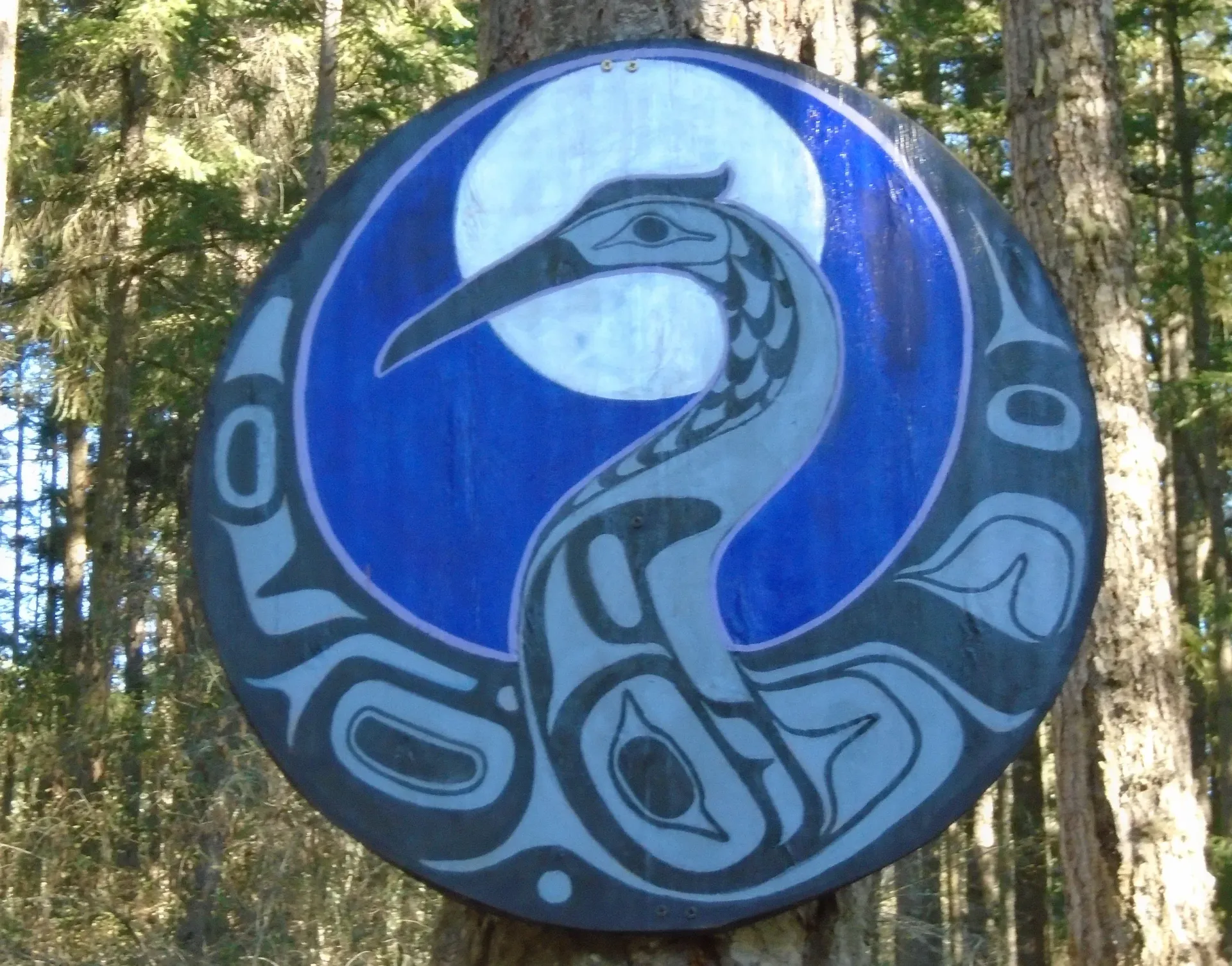 Blue circular sign with a stylized bird design against a wooded background