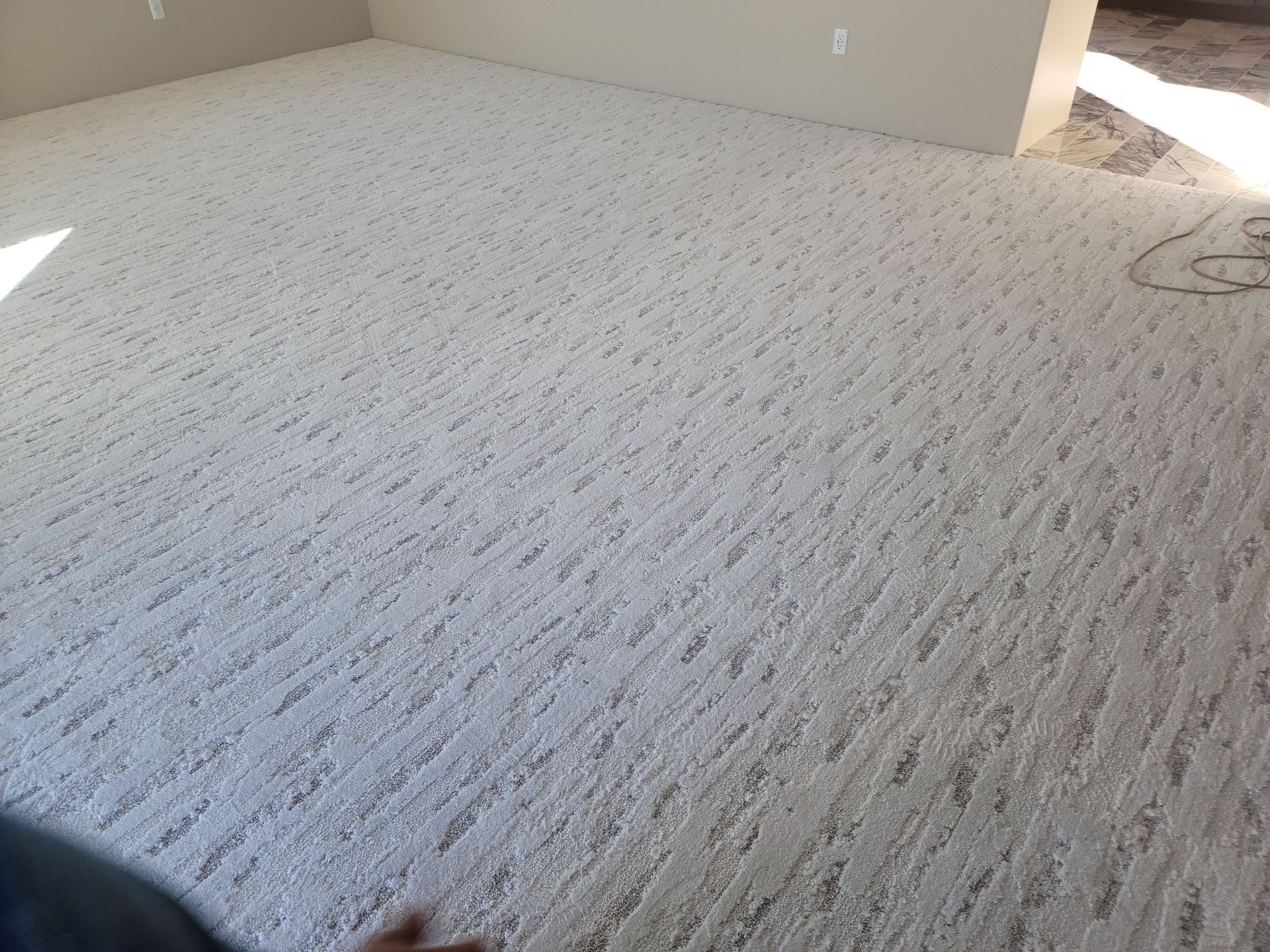 Empty carpeted room with light gray patterned carpet and beige walls near a bright doorway