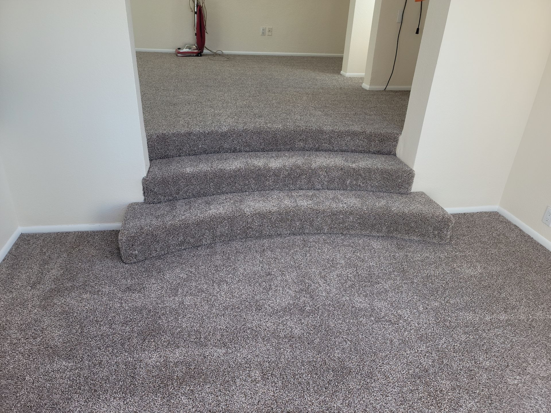 Carpeted indoor steps leading to a hallway with white walls and a red fire extinguisher in the distance