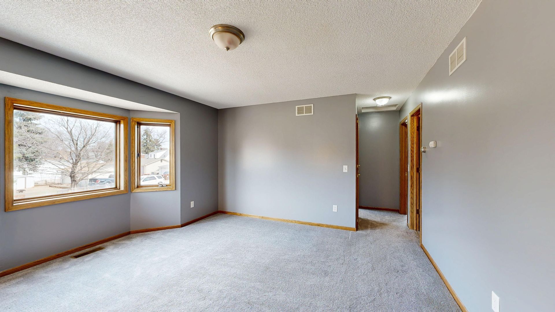 Empty gray bedroom with carpet, large window, and an open doorway