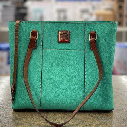A green purse with brown straps is sitting on a table.
