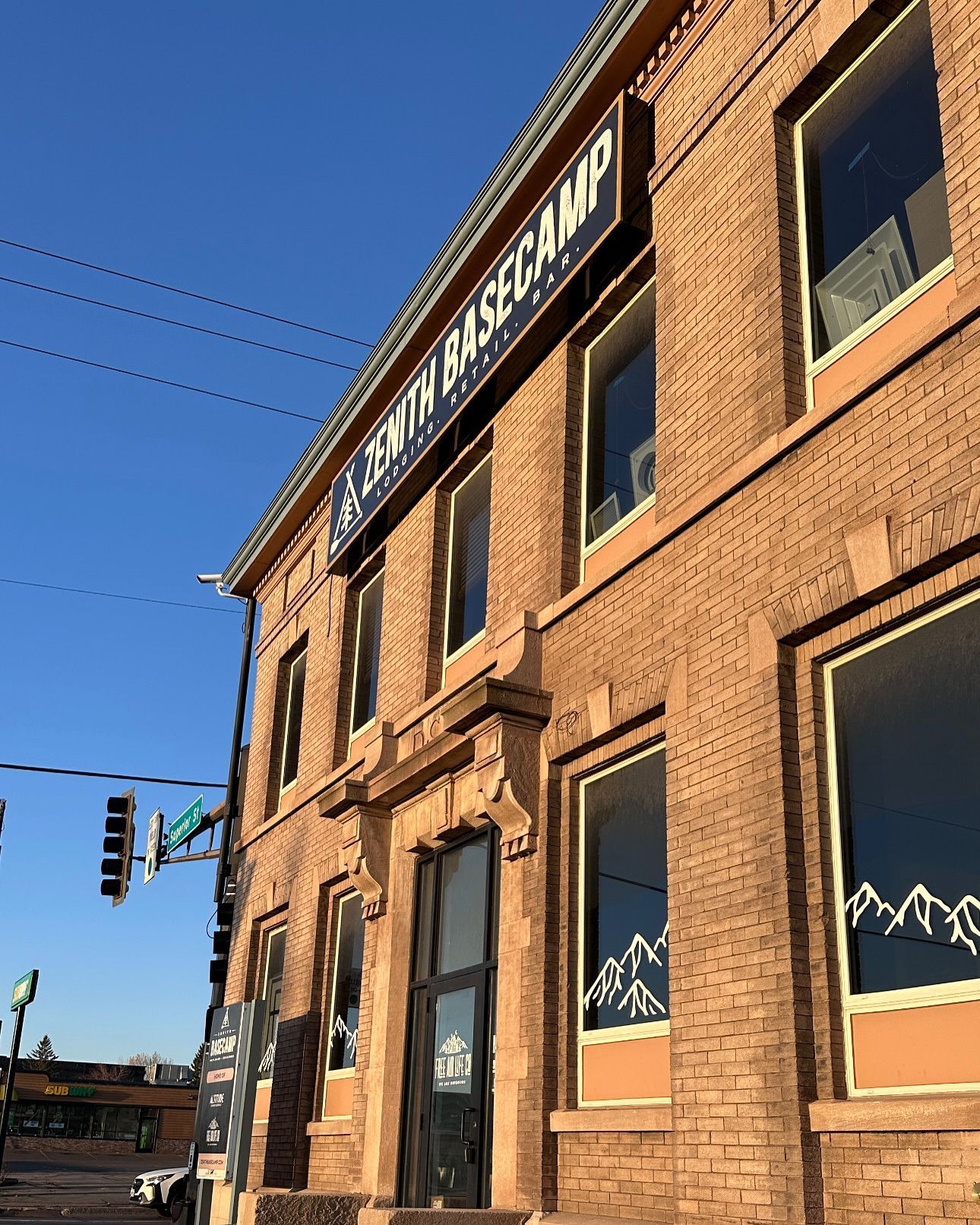 Brick building with a sign that reads “Zenith BASECAMP,” clear blue sky, mountain logo on windows.