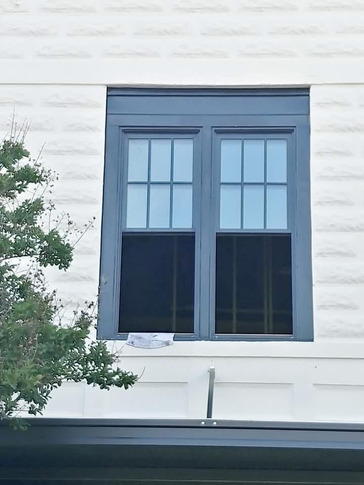 Blue-framed window with divided panes, set in a white brick wall. Dark screens cover the window.