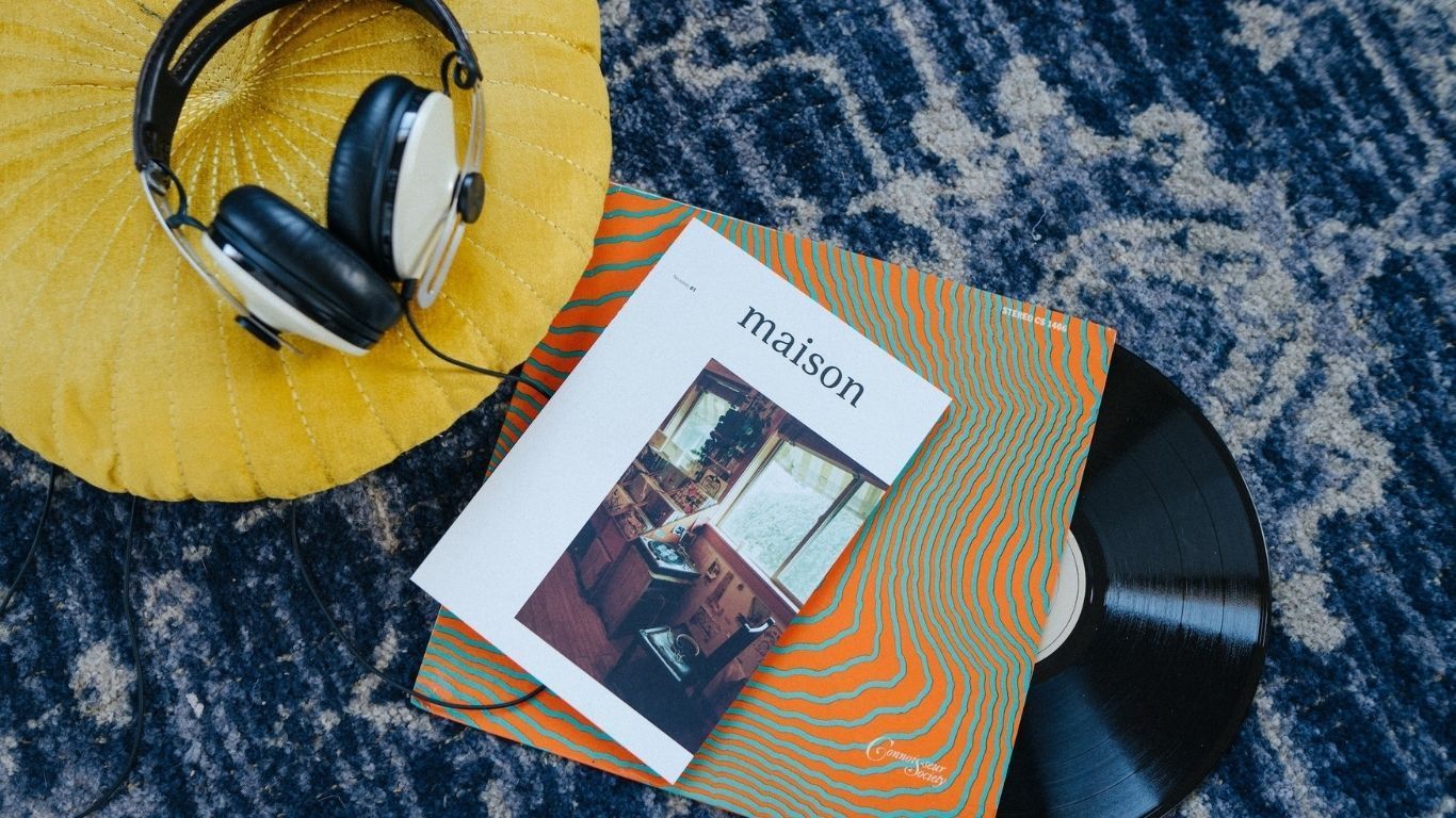 Headphones on a yellow cushion next to a magazine and a vinyl record on a patterned blue rug.