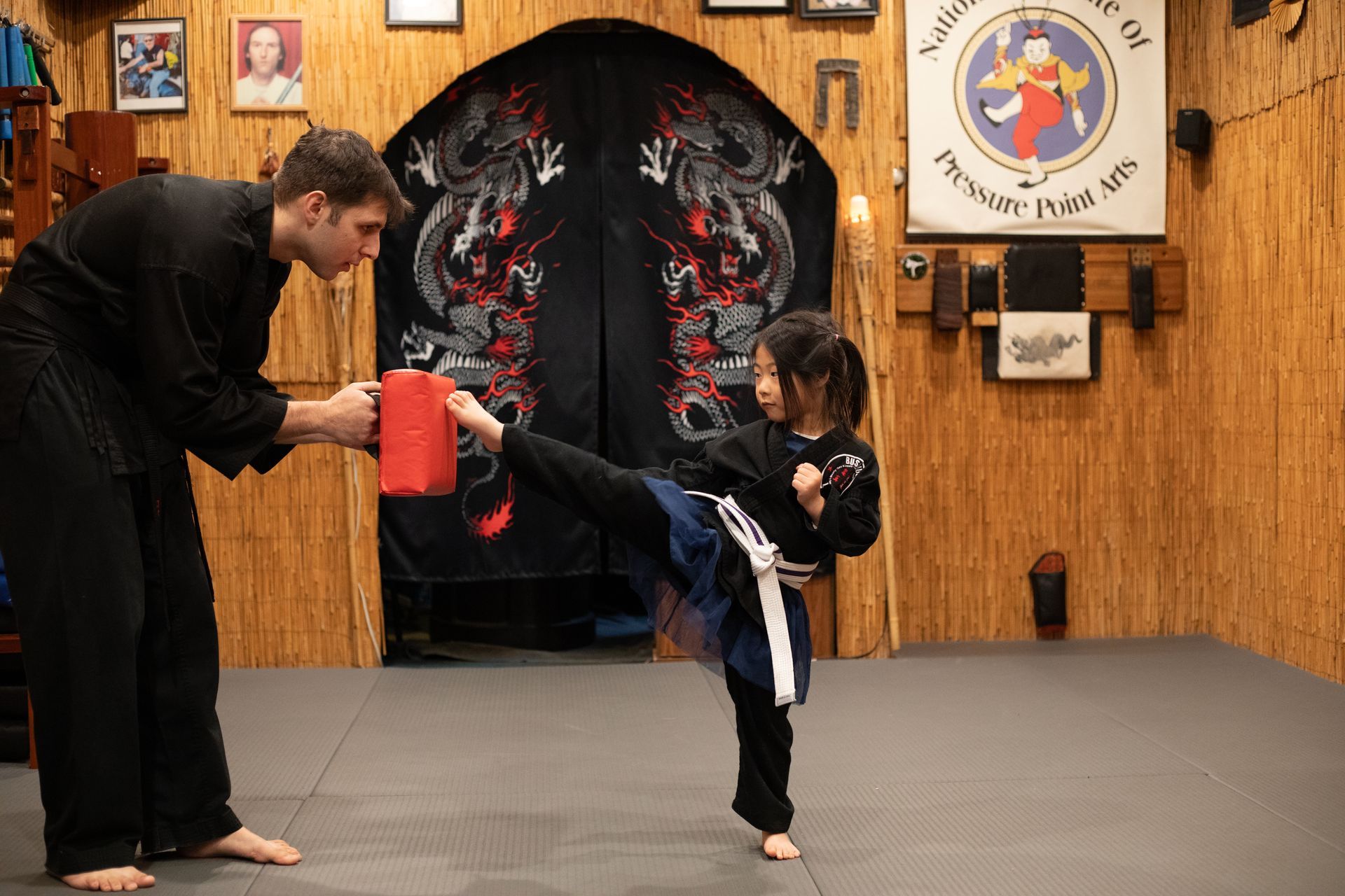 A man is teaching a little girl how to kick in a martial arts gym.