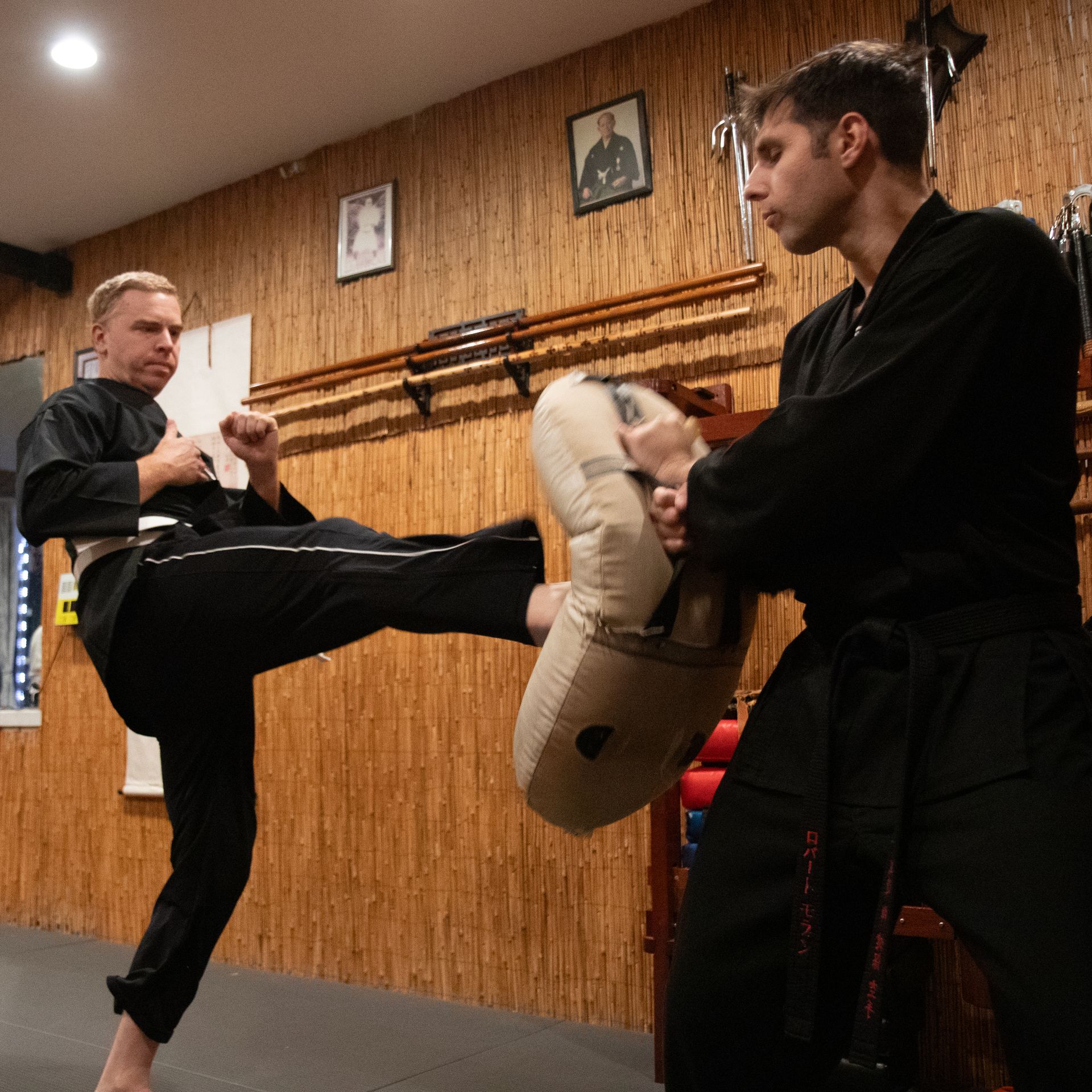 Two men are practicing martial arts in front of a wooden wall