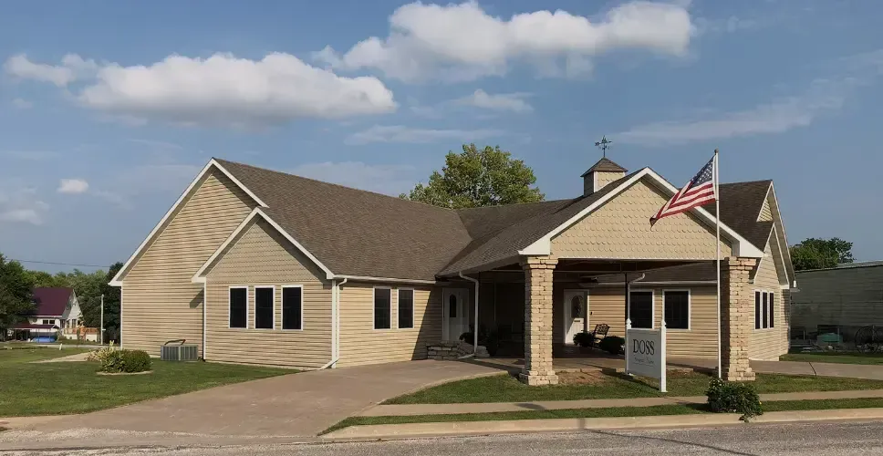 Single-story beige building with a covered entrance and an American flag in front under a partly cloudy sky