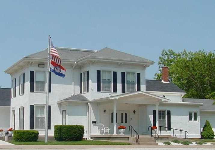 White two-story house with black shutters and a porch, flying an American and New Jersey flag.
