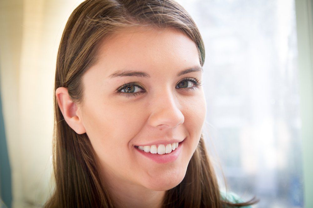 A young woman is smiling for the camera in front of a window.