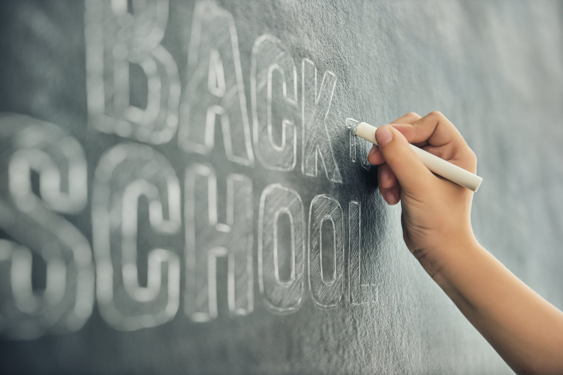A person is writing the word back school on a blackboard.