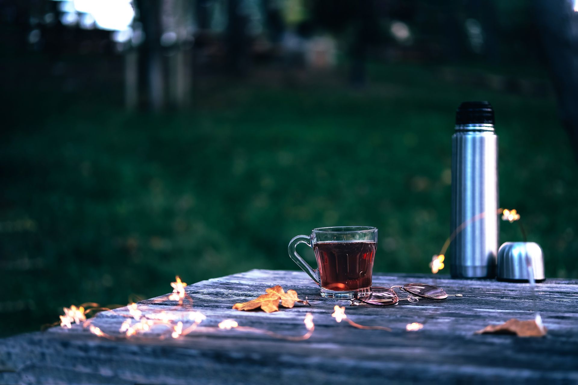 A cup of tea and a thermos are on a wooden table.