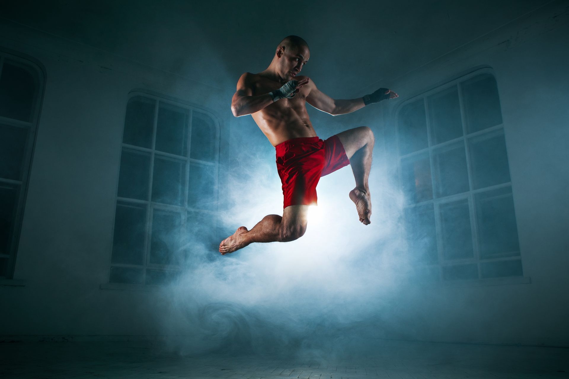 A man in red shorts is jumping in the air in a dark room.