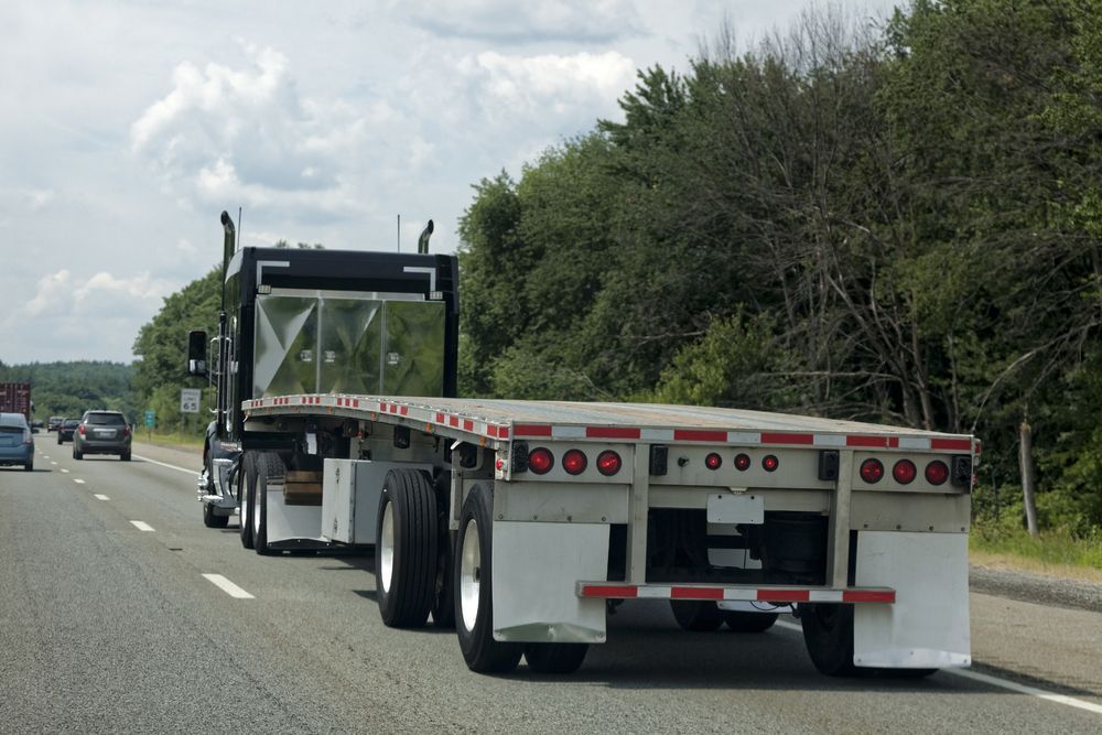 A semi truck with a flatbed trailer is driving down a highway.