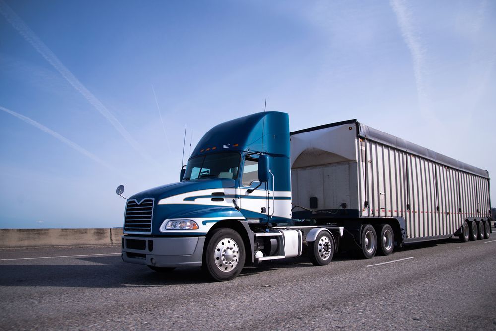 A blue semi truck is driving down a highway with a trailer attached to it.