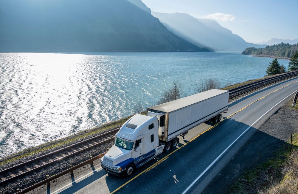 A semi truck is driving down a highway next to a lake.