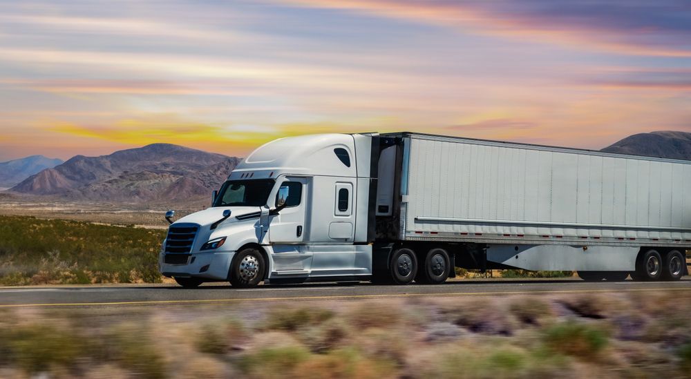 A white semi truck is driving down a desert road.