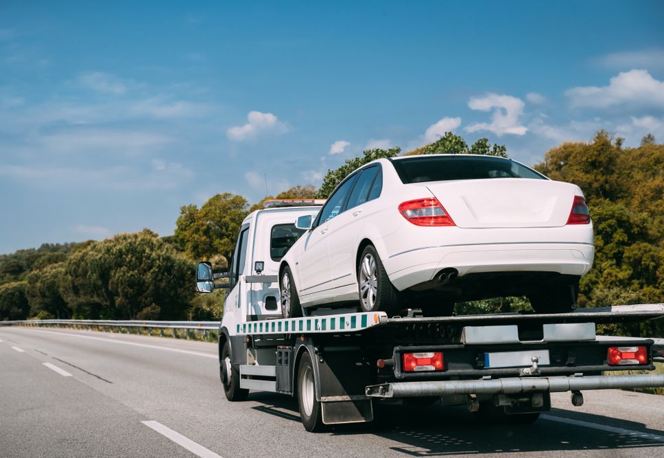 A tow truck is towing a white car on a highway.