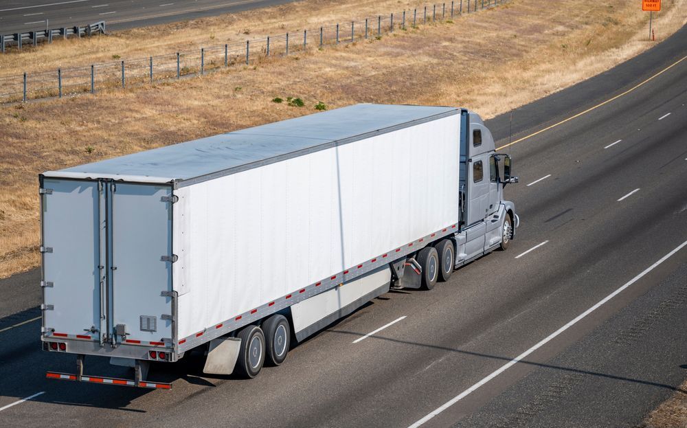 A semi truck with a white trailer is driving down a highway.