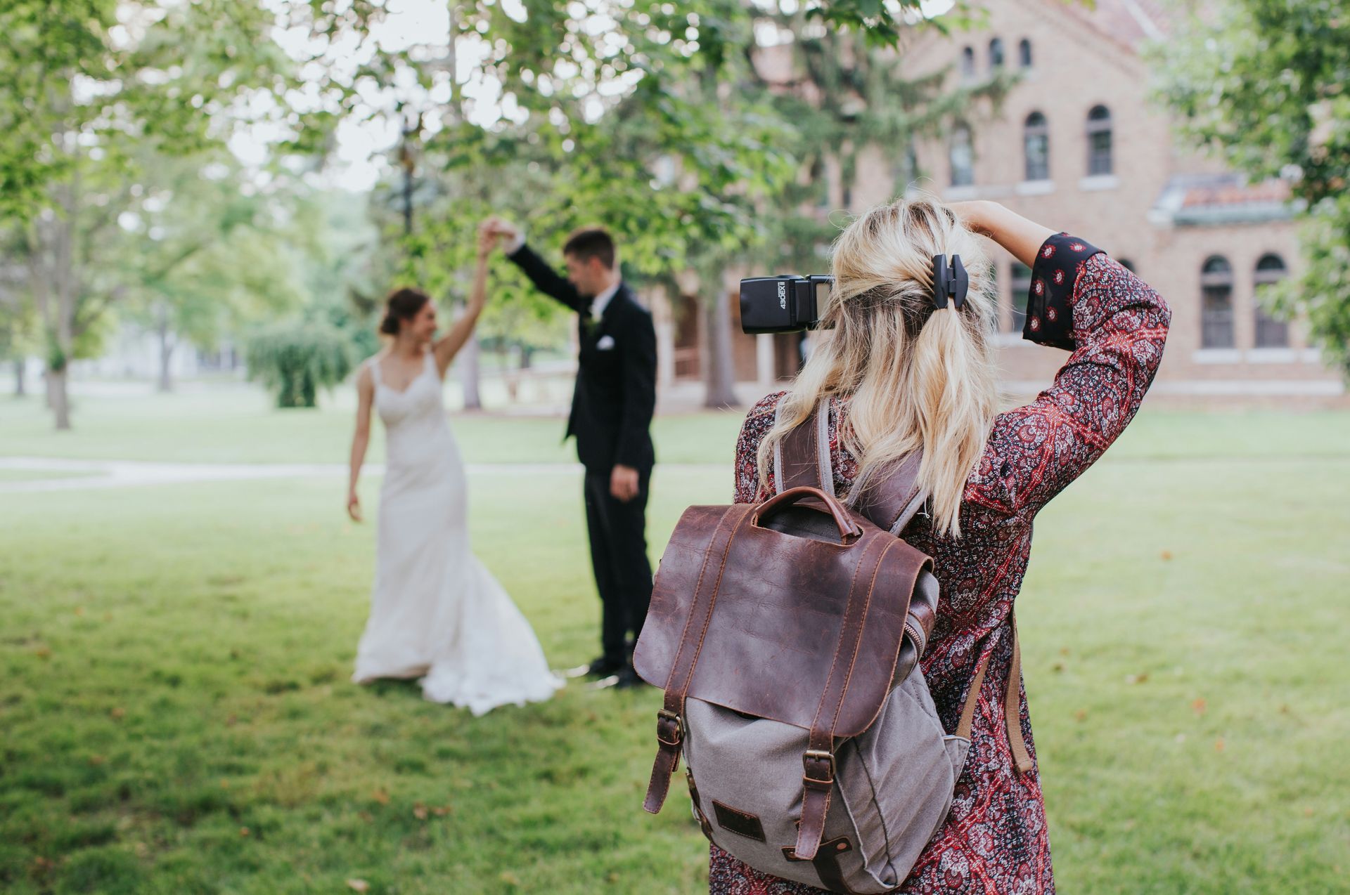 A woman is taking a picture of a bride and groom in a park.