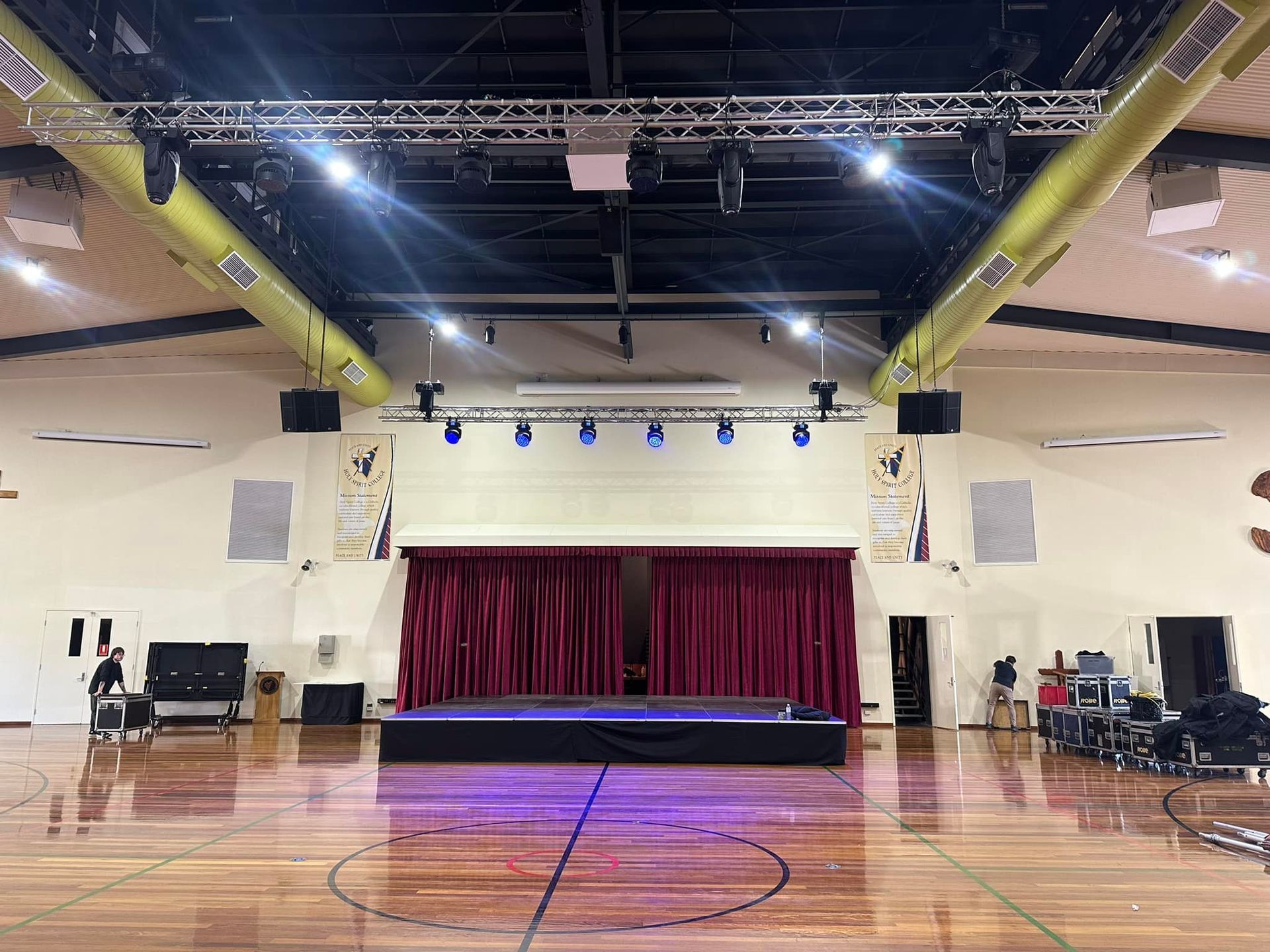 Stage In A Gymnasium With Red Curtains, Lighting Rigs, And Wooden Floor — Kennedy Amplifier Hire Service In South Mackay, QLD