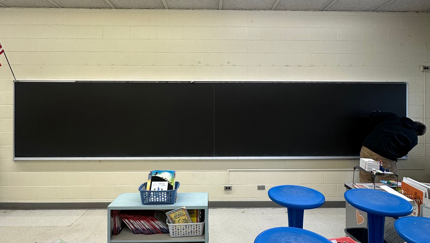 Empty classroom with a large blackboard, small table, and blue stools in front.